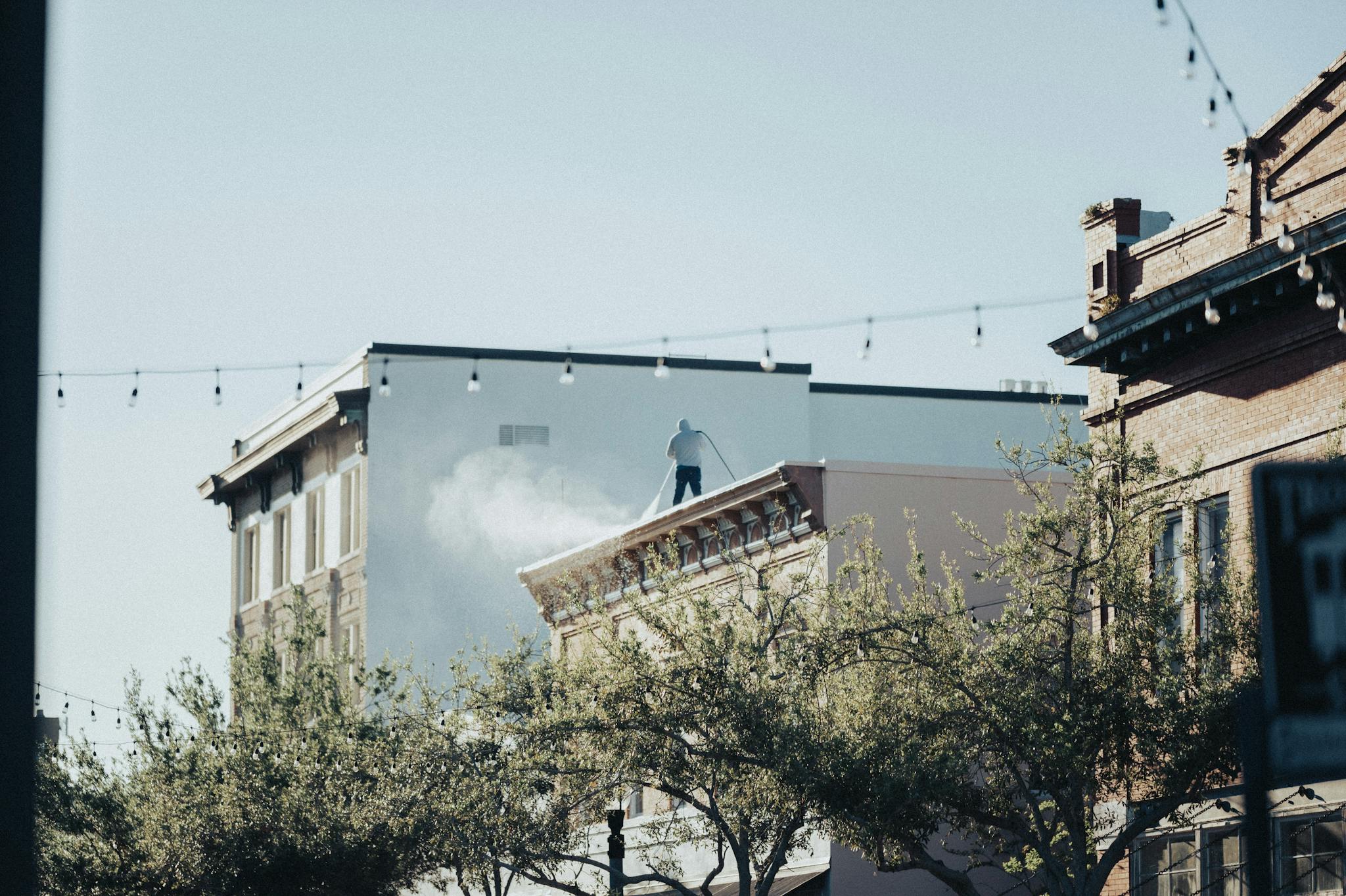 A worker stands on a rooftop in an urban setting, surrounded by vintage architecture.